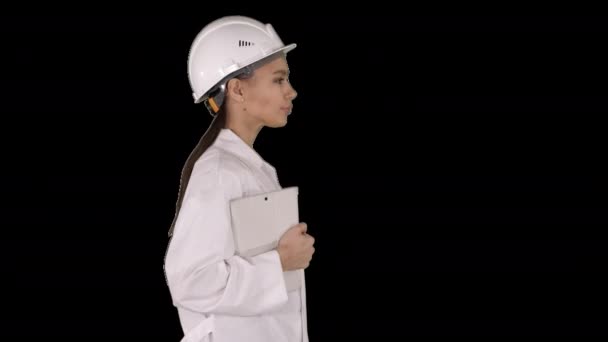 Attraktiv spansktalande kvinna i vit labbrock och vit säkerhet hårt hatt promenader håller anteckningsbok eller tablett, Alpha Channel — Stockvideo
