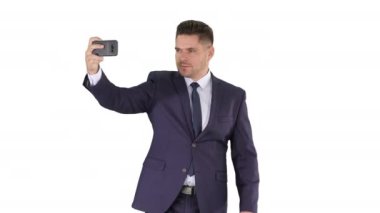 Takım elbiseli yakışıklı adam beyaz arka planda yürürken selfie çekiyor..