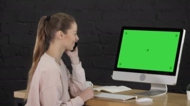 Pembe rahat giysiler içinde Sevimli kadın bilgisayar monitörü önünde bir arama yapma. Yeşil Ekran Mock-up Ekran.