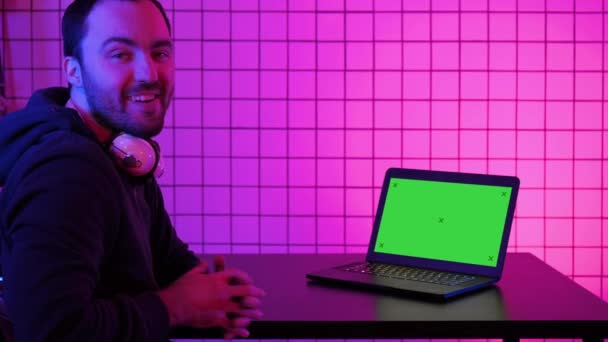 En ung glad Gamer leende till kameran och titta på laptop. Grön skärm mock-up display. — Stockvideo