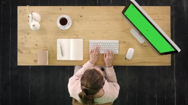 Mladé děvče z oddělení služeb zákazníkům, které nosí sluchátka a pracují na počítači. Obrazovka se zelenou obrazovkou. — Stock video