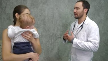 Çocuk doktorları ofisinde annesi olan çocuk bir doktorla konuşuyor.