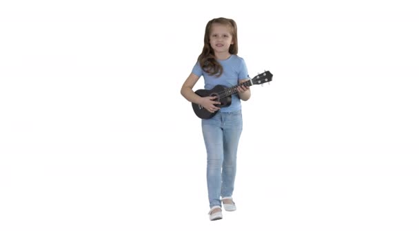 Bambina che canta e suona la piccola chitarra mentre cammina verso la fotocamera su sfondo bianco . — Video Stock