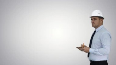 Kasklı adam ve resmi kıyafetler etrafa bakıyor ve degrade arka plan üzerine notlar alıyor.