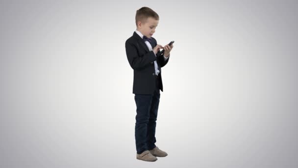 Мальчик в элегантном костюме играет с мобильным телефоном на градиентном фоне . — стоковое видео