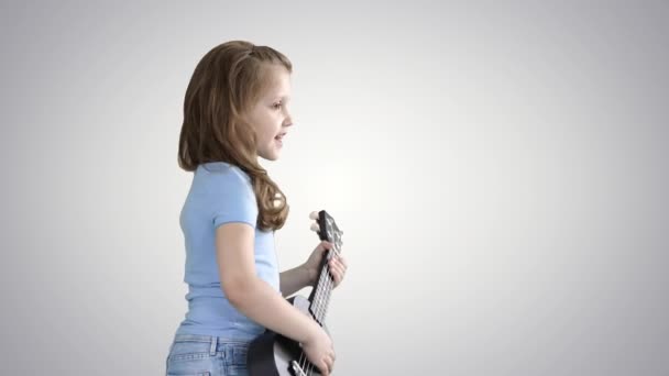グラデーションの背景にウクレレで遊んでいる間、かわいい女の子が歩いて歌う. — ストック動画