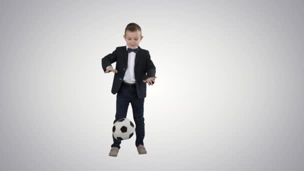 Menino em um terno formal chutando futebol no fundo gradiente . — Vídeo de Stock