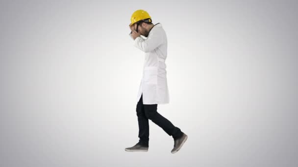 Молодий інженер-будівельник ходить і кладе шапку на градієнтному фоні . — стокове відео