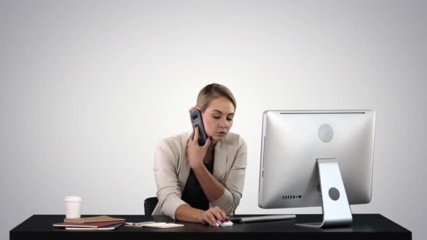 Prachtige vrolijke glimlachende jonge kantoorvrouw die op de computer aan het bureau werkt Aantrekkelijk vrolijk model in formele kleding met smartphone en computer, bellen tijdens de werkdag op een gradiënt achtergrond. — Stockvideo