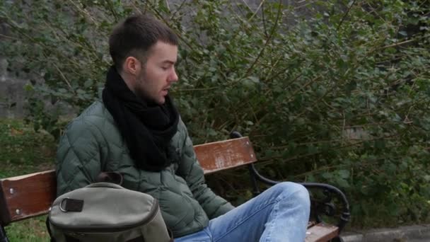男はベンチで朝タバコを吸う。天気は寒い。. — ストック動画