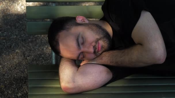 Joven acostado durmiendo en el banco en el parque y se despierta después del descanso — Vídeos de Stock