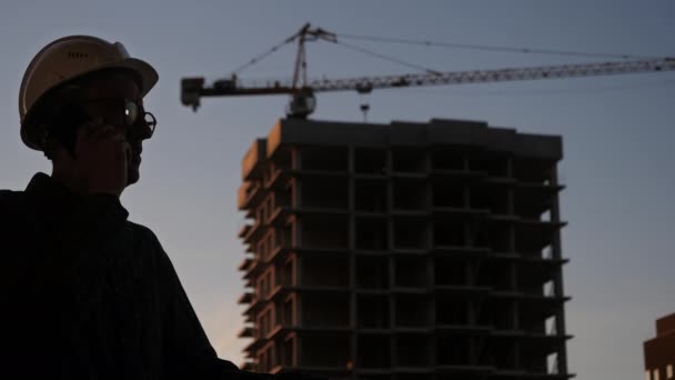 Ingegnere con un cappello bianco che parla al telefono. Silhouette . — Video Stock