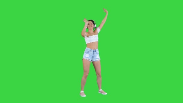 Modelo femenino caucásico en auriculares saltando, expresando emociones felices escuchando música en una pantalla verde, Chroma Key. — Vídeo de stock