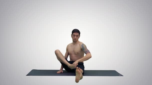 Молодий чоловік практикує йогу в наполовину героя розтягує позу на градієнтному фоні . — стокове відео