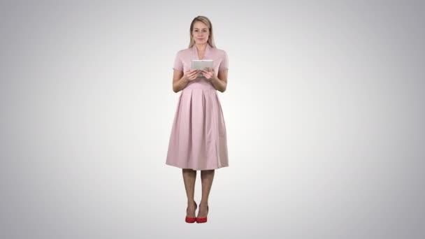 Ganska charmig säker trendig kvinna i rosa med tablett i händerna tittar på kameran och vända sidor eller spyr knappar på fliken på lutning bakgrund. — Stockvideo