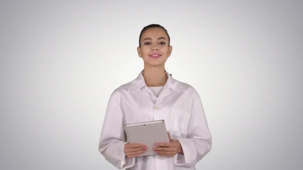 Happy female doctor using tablet computer swiping pages on it on gradient background. — Stock Video