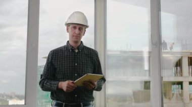 Hardhat'ta üst düzey mühendis tablette kaydırma ve bir şey sunan kameraya bakma.