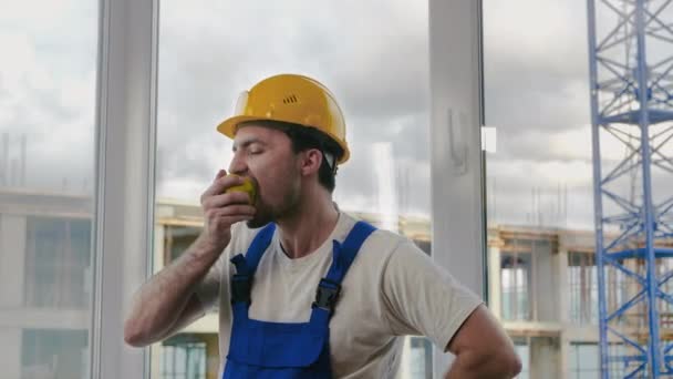 Jonge man bouwvakker die een appel eet. — Stockvideo