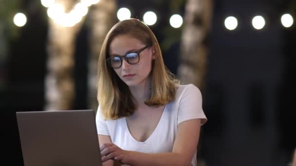 Jovem mulher de negócios casual em óculos com laptop trabalhando à noite fora. — Vídeo de Stock