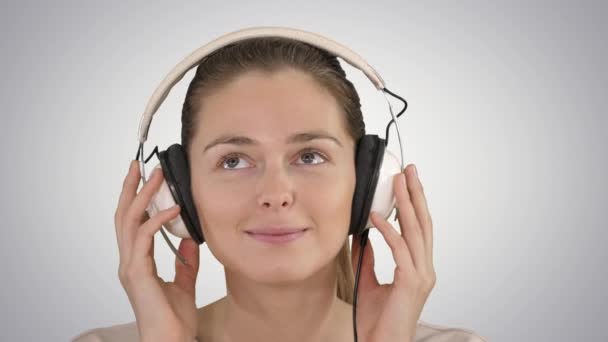 Mujer encantadora sonriendo mientras escucha música en auriculares sobre fondo degradado . — Vídeos de Stock