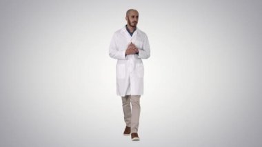 Tıp üniforması giyen orta yaşlı bir doktor, arka plandaki kameraya bakarak avuç içini gösteriyor ve işaret ediyor..