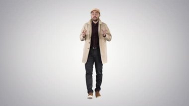 Trençkot giyen genç adam degrade arka planda kameraya konuşuyor.