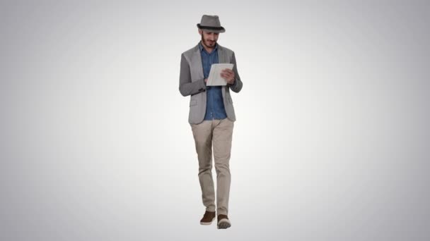 Handsome smiling arab man in a hat walking and using tablet on gradient background. — Stock Video