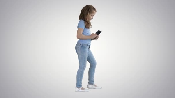 Little girl is playing with smartphone while walking on gradient background. — Stock Video