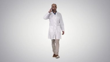 Degrade arka planda yürürken cep telefonu yla konuşan profesyonel tıp doktoru.