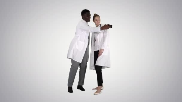 Twee artsen maken selfie met behulp van een smartphone en glimlachen op gradiënt achtergrond. — Stockvideo
