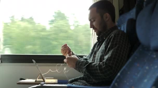 Człowiek rozwikłać białe małe słuchawki na wycieczkę pociągiem. — Wideo stockowe