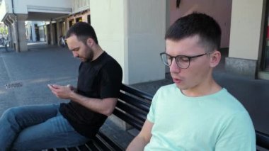 Bankta sigara içen gözlüklü yakışıklı hippi telefon kullanan başka bir adamın yanında..