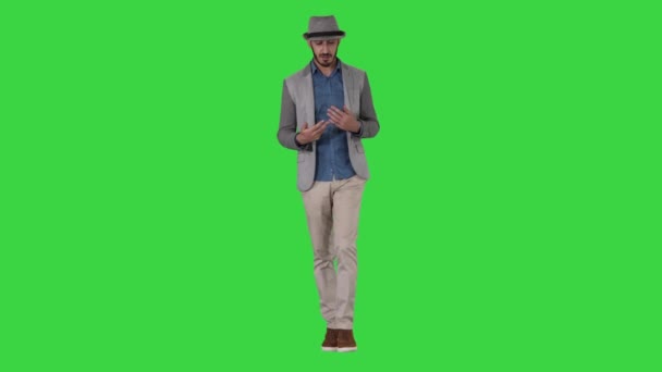 Trendy stylische positive fröhliche Mann trägt lässiges Hemd und Sonnenhut zu Fuß und im Gespräch mit der Kamera auf einem grünen Bildschirm, Chroma-Schlüssel. — Stockvideo