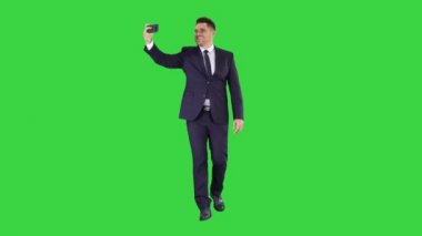 Yeşil Ekranda yürürken selfie çeken takım elbiseli yakışıklı adam, Chroma Key.