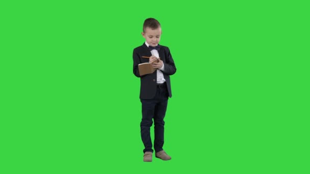 Pojke i en formell kläder skriver i Checklista eller anteckningsbok på en grön skärm, Chroma Key. — Stockvideo