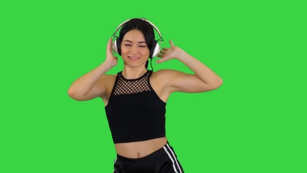 Jonge vrolijke sportieve vrouw die muziek luistert in hoofdtelefoon en danst op een groen scherm, Chroma Key. — Stockvideo