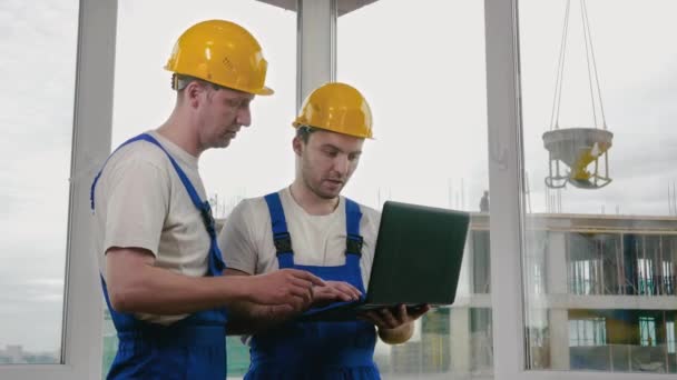 Dos constructores con cascos protectores trabajando en un portátil. — Vídeos de Stock