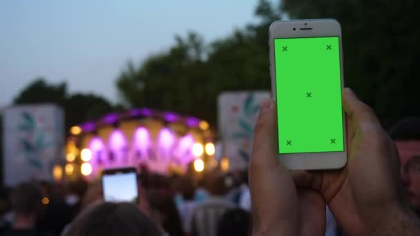 Hand av ung man som innehar telefon inspelnings video framför suddig konsert bakgrund. — Stockvideo