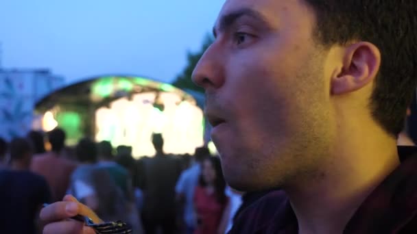 Seorang pria makan makanan cepat saji di festival . — Stok Video