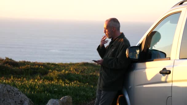 Cabo da Roca, Potugal-27 december 2017: man roken met een telefoon in een hand staande door de auto. — Stockvideo