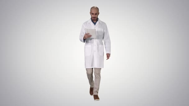 Dojrzały mężczyzna lekarz trzyma cyfrowy tablet przy pomocy ono i chodzenie na gradient tło. — Wideo stockowe
