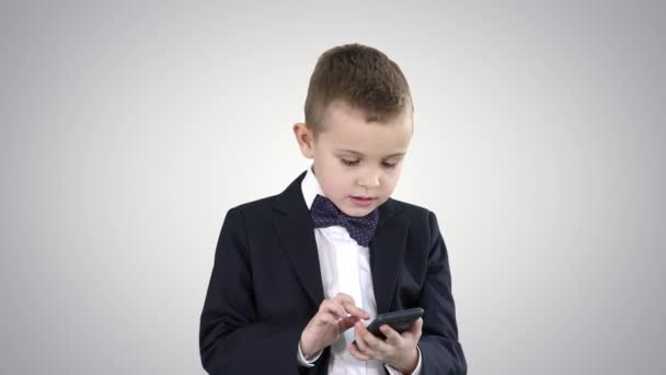 Intelligenter Junge schreibt SMS, spielt Online-Spiele, verschickt Bilder, lädt Musik, Filme auf Gradienten-Hintergrund herunter. — Stockvideo