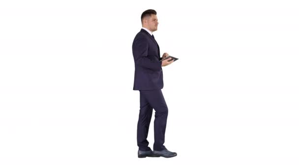 Elegante jonge zakenman met behulp van zijn PC tablet tijdens het lopen op een witte achtergrond. — Stockvideo