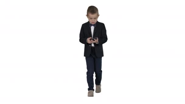 Menino pequeno no traje andando e usando smartphone no fundo branco . — Vídeo de Stock