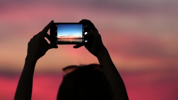 Mulher tirando fotos com seu smartphone ao pôr do sol . — Vídeo de Stock