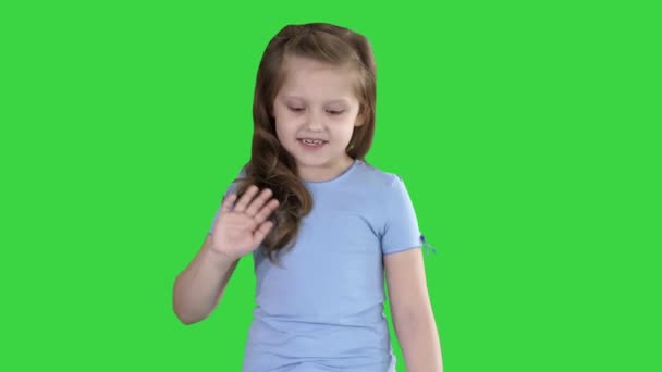 Χαρούμενος χαριτωμένο μικρό yyvyτο κούνημα του χεριού λέγοντας Γεια Hi κοιτάζοντας την κάμερα μιλάει και περπάτημα σε μια πράσινη οθόνη, πλήκτρο αποχρώσεων. — Αρχείο Βίντεο