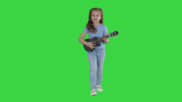 Niña cantando y tocando la pequeña guitarra mientras camina hacia la cámara en una pantalla verde, Chroma Key . — Vídeos de Stock