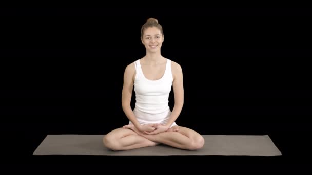 Hermosa mujer en ropas blancas sentada en una esterilla de yoga y hablando con la cámara, Alpha Channel — Vídeos de Stock