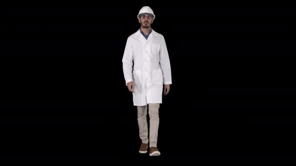 Mladý inženýr v županu a helmě, který při chůzi dává brýle, alfa kanál — Stock video