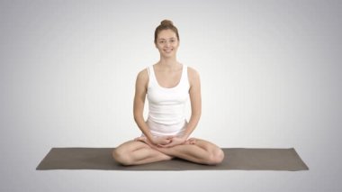 Yoga minderinüzerinde oturan ve degrade arka planda kamera ile konuşurken beyaz clothers güzel kadın.